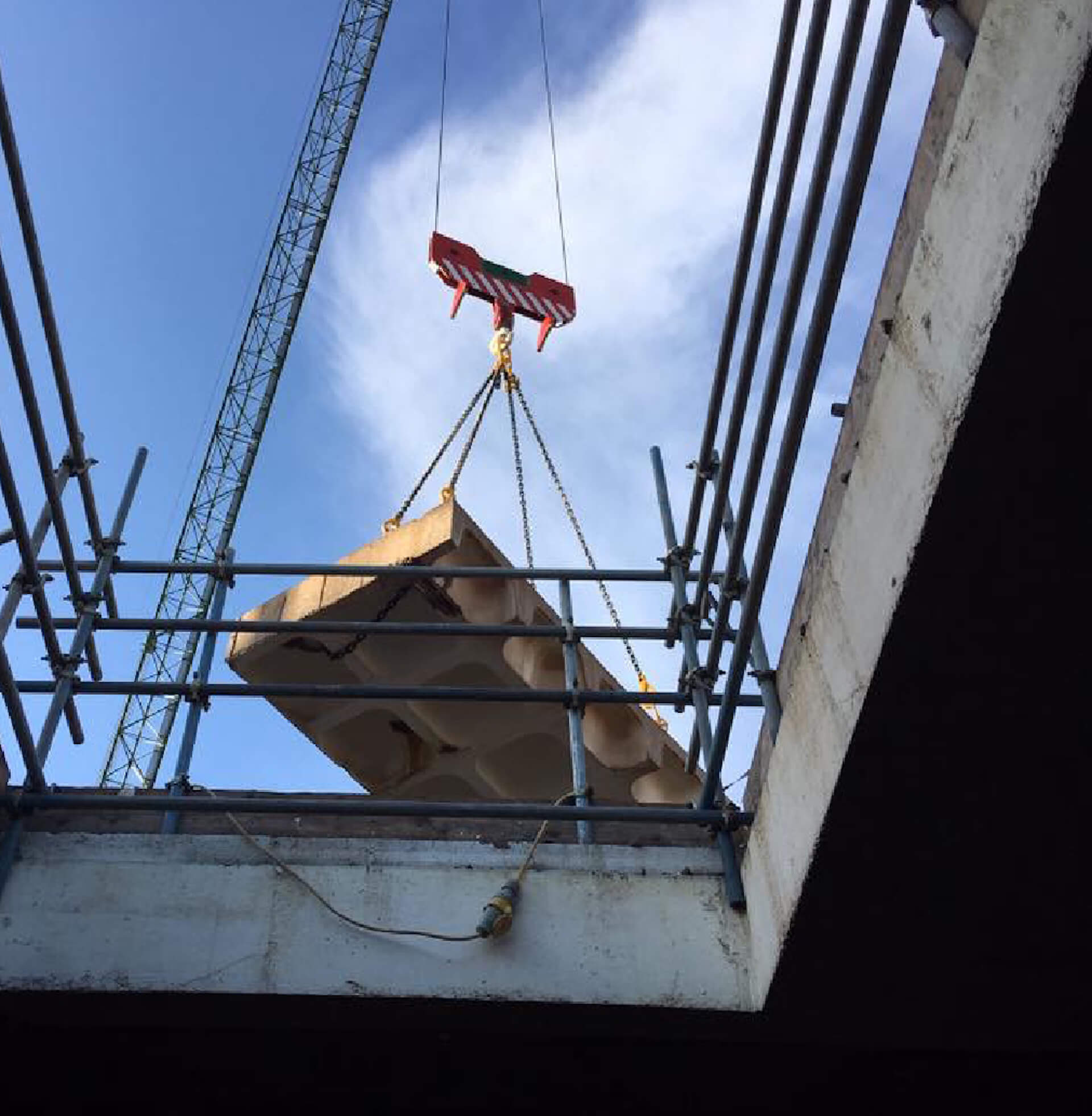 upward view of concrete slab being lifted from the site by crane.