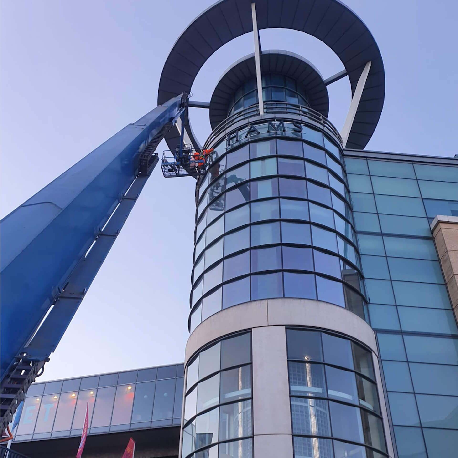 sky view of a Debenhams store's glass round shaped building. A crane is next to it with a worker on the crane lift.