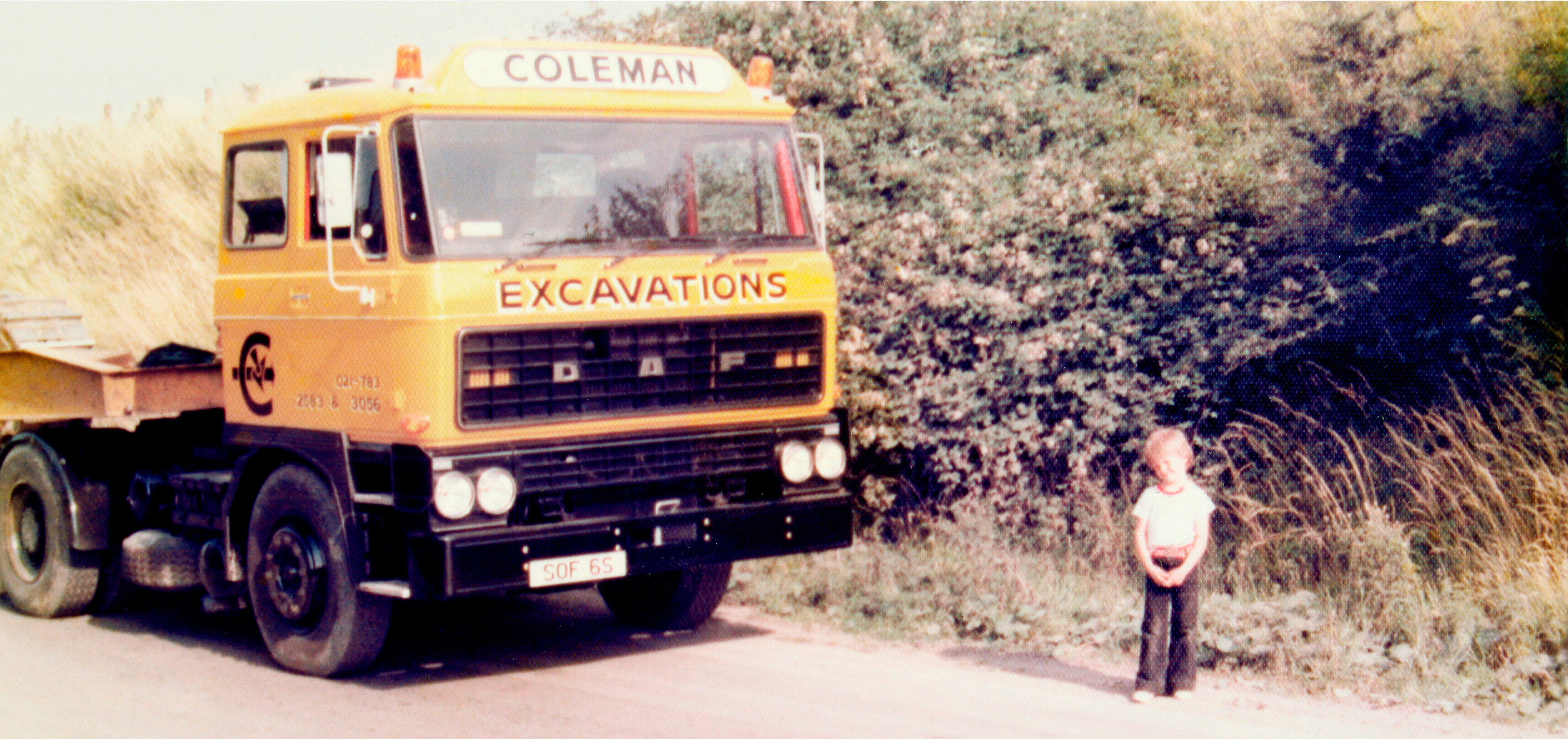 Image of Mark Coleman as a small child stood outside next to a yellow van with Coleman branding on it.