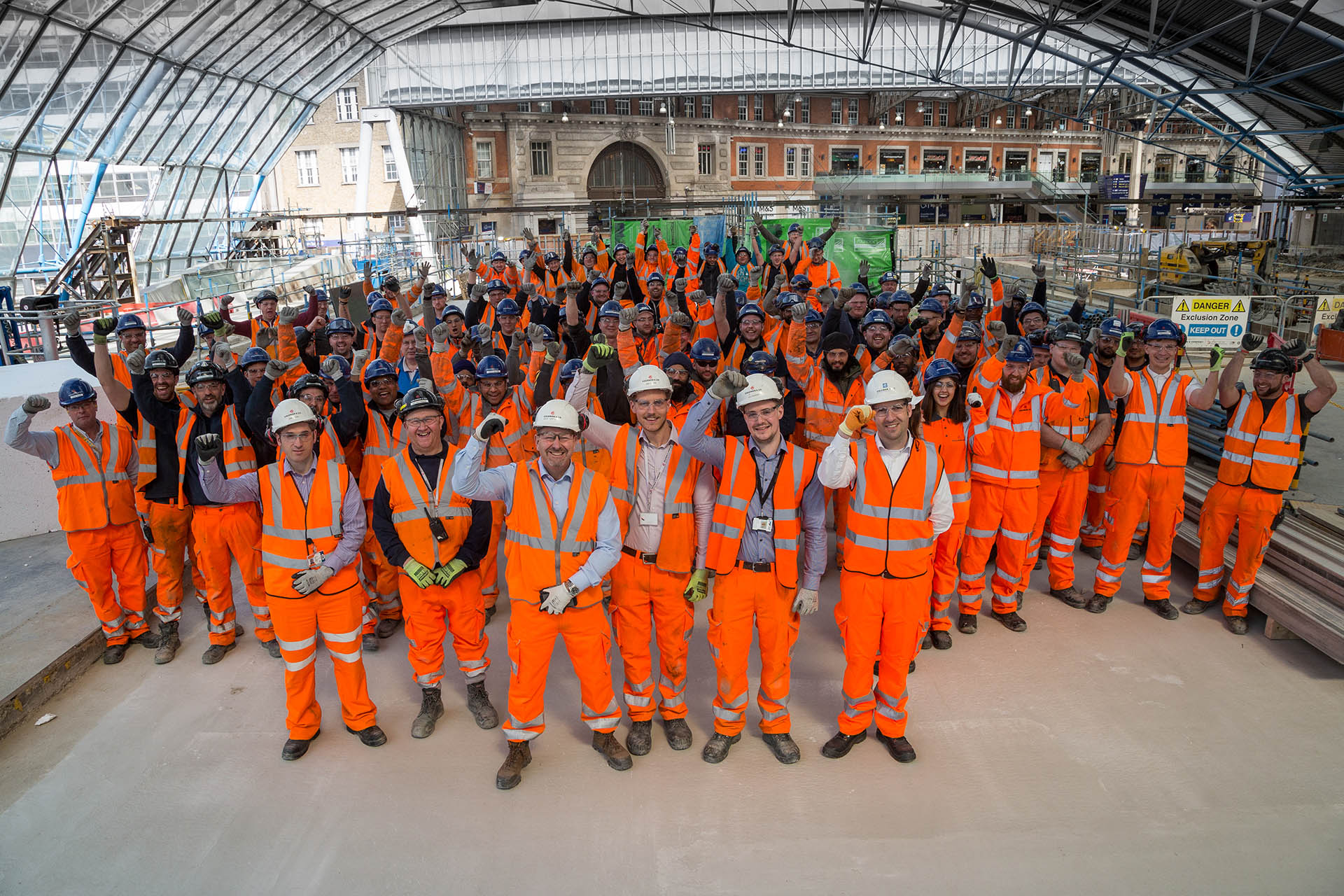 image of a large team of site people smiling for a picture on a demolition site. All workers are wearing colemans high visibility safety wear.