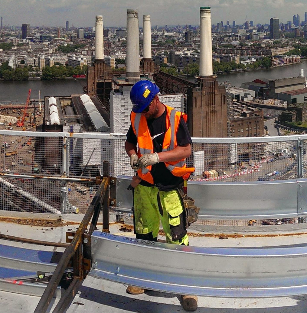 man working on top of battersea gas holder. Battersea power station and London view in the background.