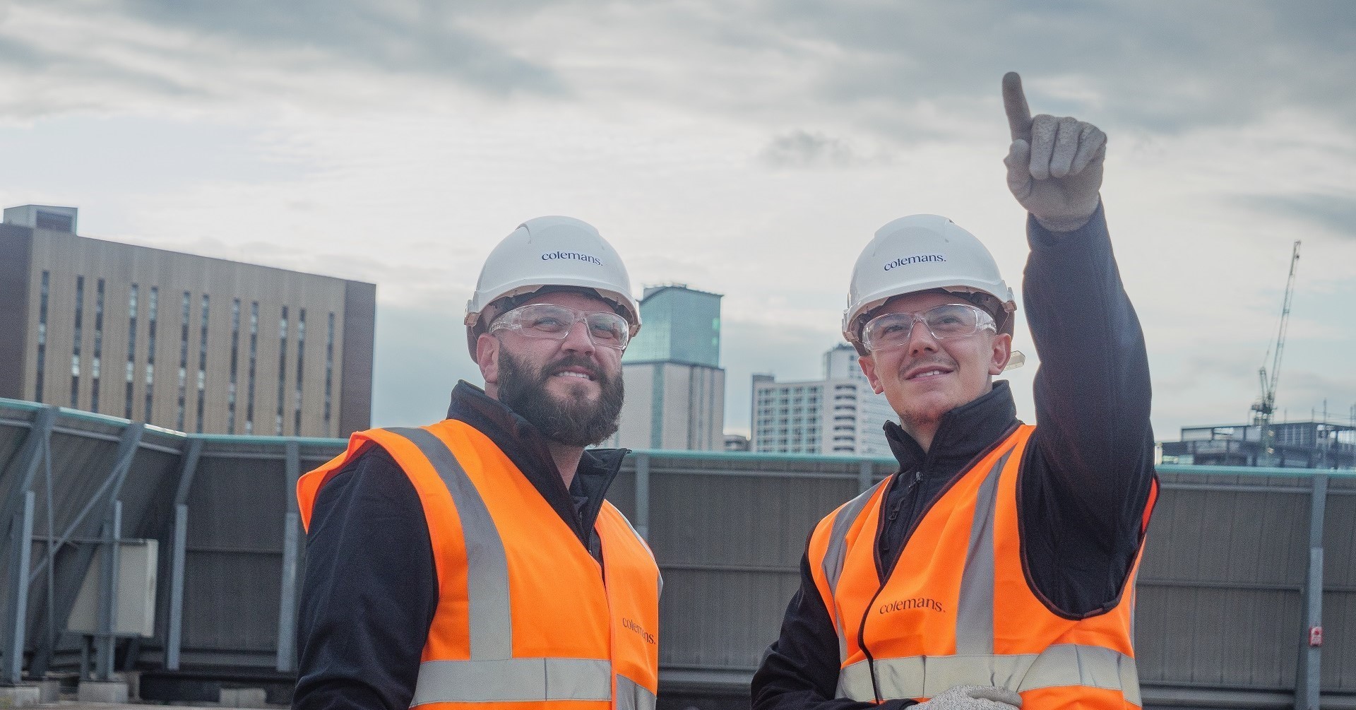 banner image of two men on a working site, wearing branded high visibility protective wear and safety hats.